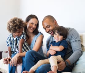 A family of four is sitting together on a couch.