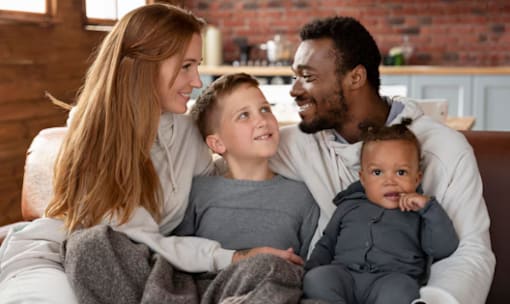 A family of four is sitting together on a couch.