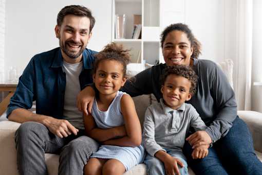 A family of four is sitting together on a couch.