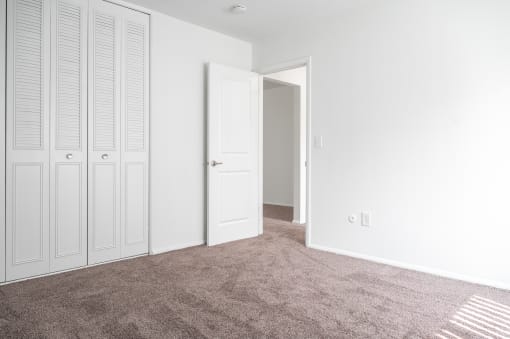 an empty bedroom with white closet doors and carpet