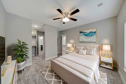 A bedroom with a large bed, a ceiling fan, and a painting on the wall.