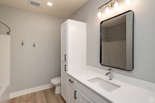 A white bathroom with a sink, mirror, and toilet.