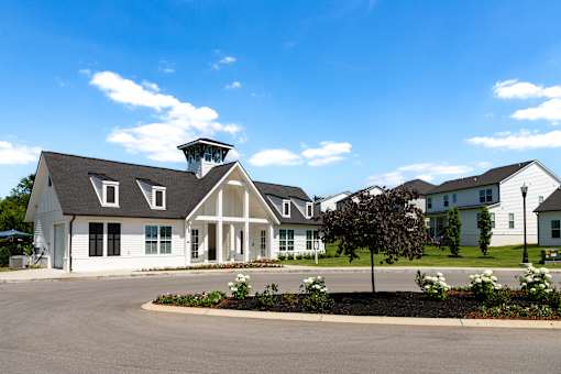 A white building with a black roof and a tower on top is surrounded by a parking lot and other buildings.