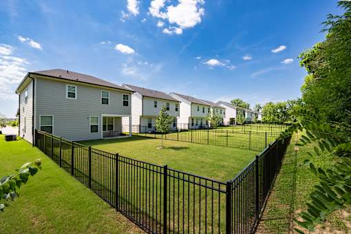 A black fence surrounds a grassy area in front of a row of houses.
