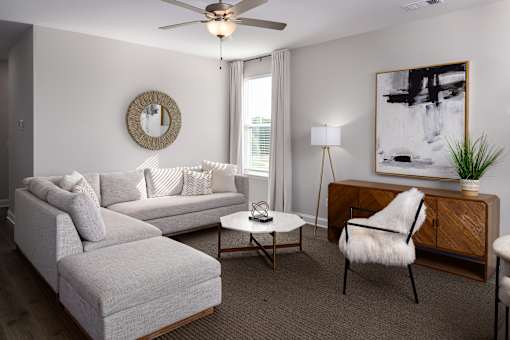 A living room with a grey couch, a white coffee table, a white chair, a wooden cabinet, and a painting on the wall.