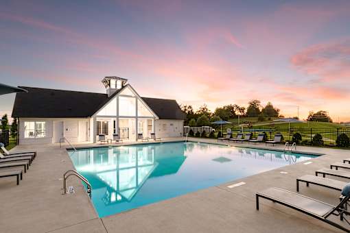 A swimming pool in front of a house with sunset in the background.