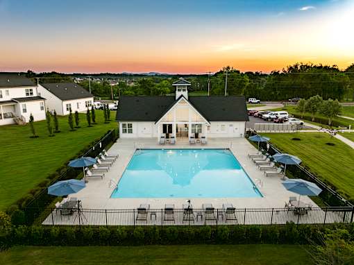 A large swimming pool surrounded by lounge chairs and umbrellas with a building in the background.