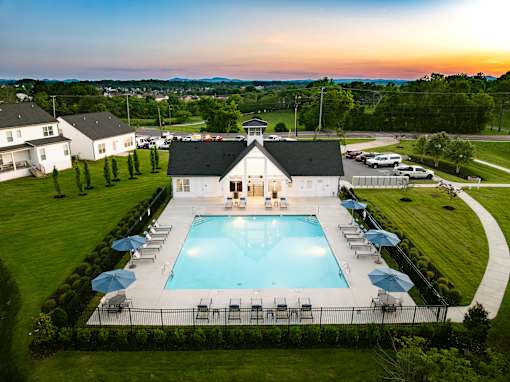 A large swimming pool surrounded by lawn chairs and umbrellas with a house in the background.