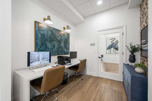A room with a desk, chairs, and a painting on the wall.