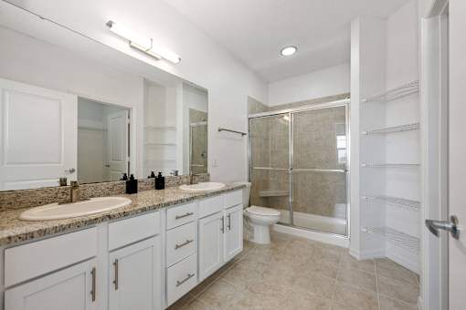 Apartments in Bradenton, FL, with In-Unit Washer and Dryer - Preserve at Riverwalk - Bathroom with Glass-Shower Doors, Large Double-Sink Vanity, Large Mirror, Shelves, Tile Flooring, and Lighting.