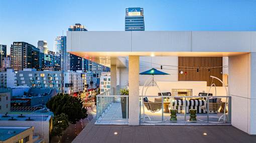 A modern balcony with a table and chairs overlooking a cityscape at dusk.