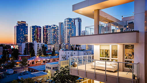A modern apartment building with a balcony overlooking a cityscape at dusk.