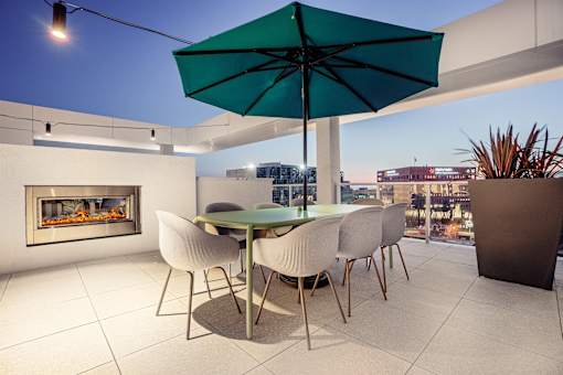 A table with chairs and an umbrella is in the foreground of a cityscape.