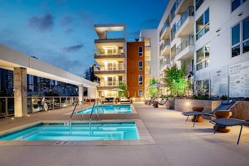 A modern pool area with a pool, loungers and a building in the background.