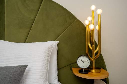 A bed with a white pillow and a gold clock on a side table.