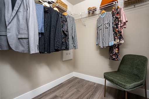 A room with a chair and clothes hanging on a rack.