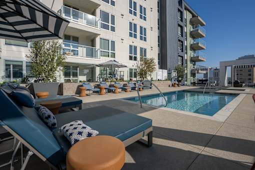 A pool area with a blue lounge chair and a brown ottoman.