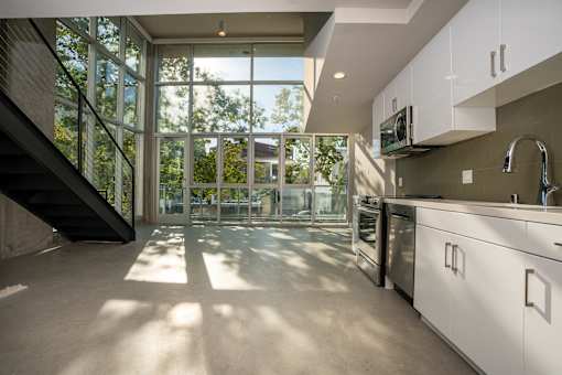 A modern kitchen with white cabinets and a staircase leading to the upper floor.