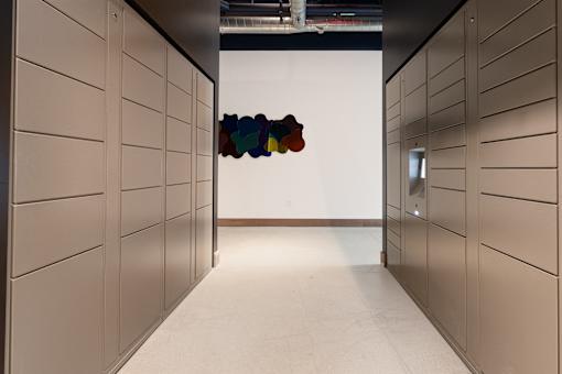 A hallway with a white wall and a row of lockers on either side.