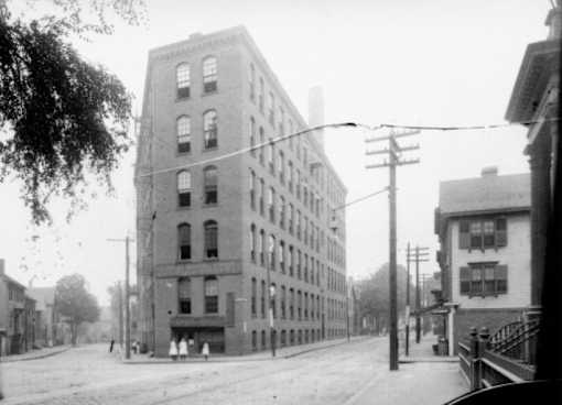 A black and white photo of a street with a large building on the left.
