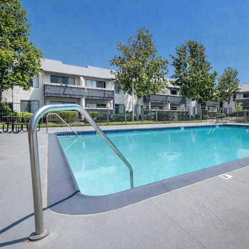 A swimming pool with a ladder in the foreground and apartment buildings in the background.