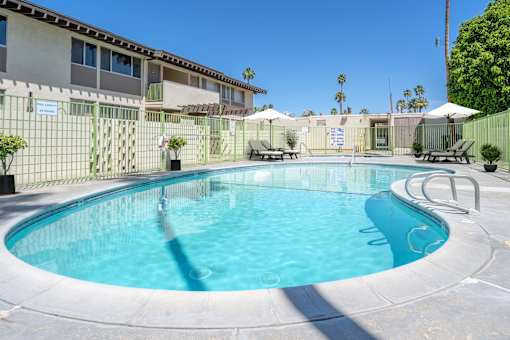 A swimming pool surrounded by a fence and lounge chairs.