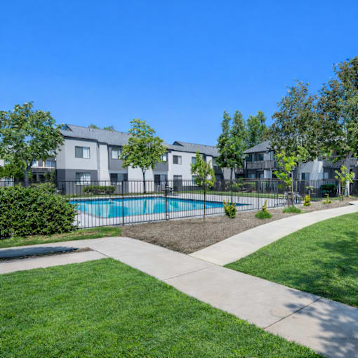 A swimming pool is surrounded by a grassy area and apartment buildings.
