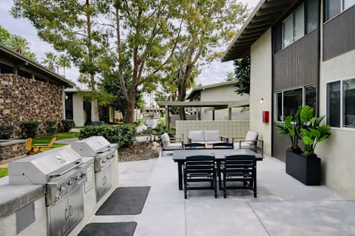 A patio with a table and chairs is surrounded by a stone wall and trees.