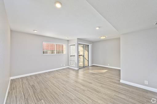 A room with light grey walls and wooden flooring with a doorway leading to another room.