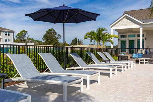 a row of lounge chairs and umbrellas on a patio with a house