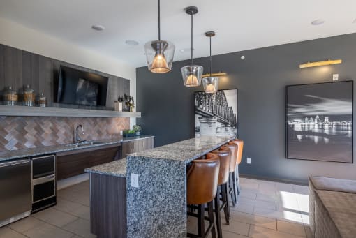 a kitchen with a long bar with chairs and a television