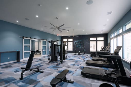 a gym with weights and cardio equipment in a large room with windows