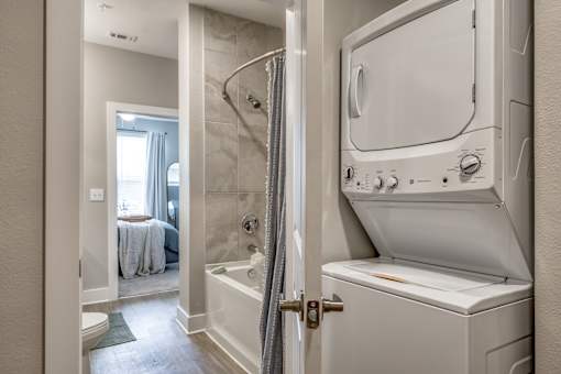 A white washing machine is in a bathroom next to a shower.