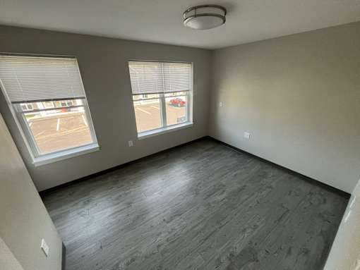 A room with grey flooring and two windows.