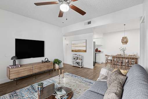 A living room with a grey sofa, a wooden coffee table, a flat screen TV, and a ceiling fan at Riviera Park, Chandler Arizona