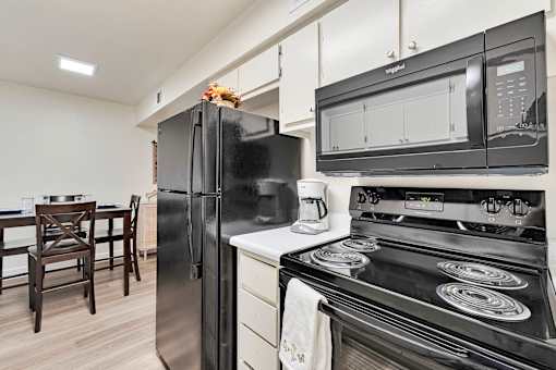 A black fridge and microwave in a kitchen with a stove and dining table.at Riviera Park, Chandler Arizona