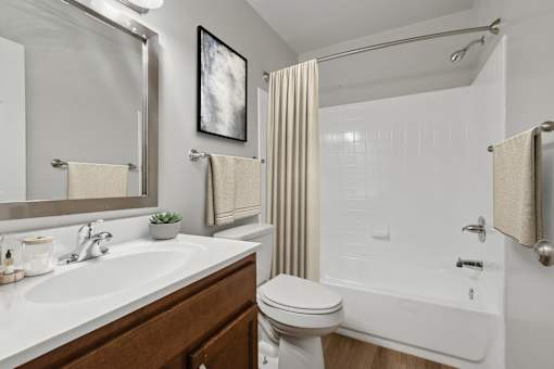 A white bathroom with a toilet, sink, and shower at Poplar Glen Apartments, Columbia, MD, 21044.