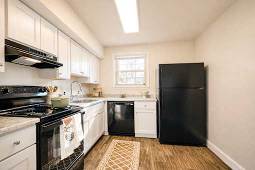 A black refrigerator stands in a kitchen with white cabinets and a black stove ighland Ridge Apartments, Capitol Heights, MD, 20743