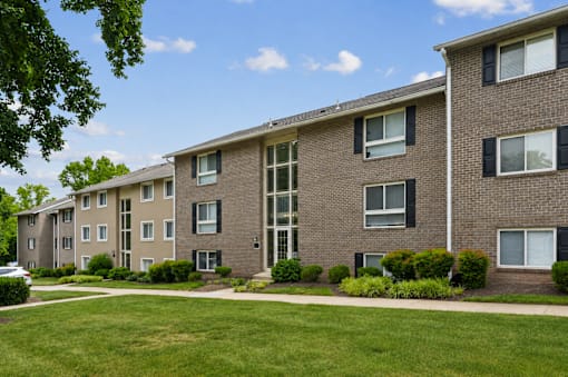 Multistory brick apartment buildings with manicured lawn at The Brook At Columbia Apartments, Columbia, MD