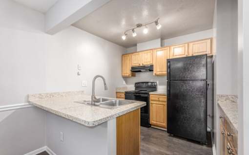 A kitchen with a black refrigerator, sink, and wooden cabinets at Madison at Eden Brook, 21046