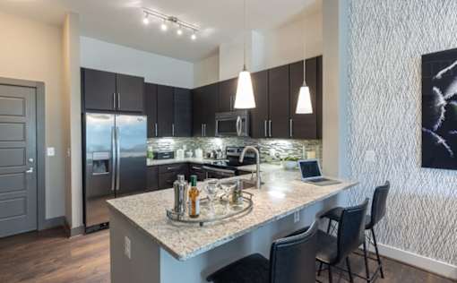 A modern kitchen with a granite countertop and stainless steel appliances at Mira Upper Rock, Maryland, 20850