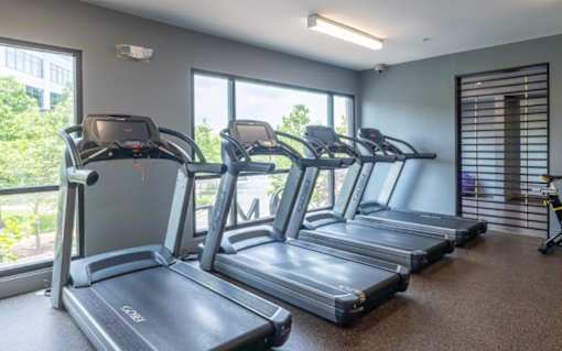 A gym with treadmills and a view of trees outside the window at Mira Upper Rock, Maryland, 20850