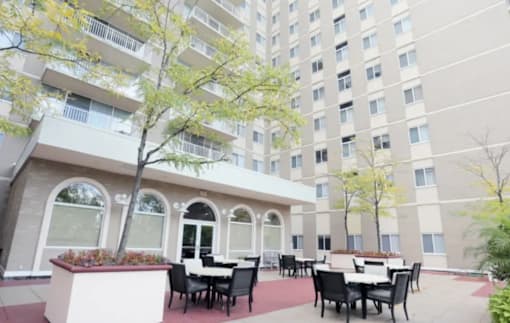 A patio with tables and chairs is surrounded by a building.