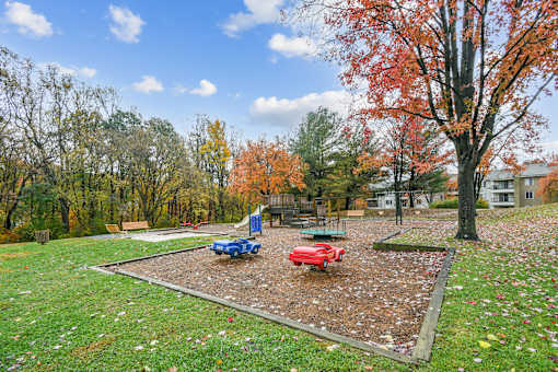 A playground with a blue slide and a red slide surrounded by trees  at Poplar Glen Apartments, Columbia, MD, 21044.