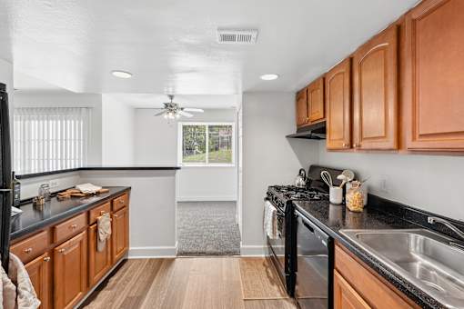 Galley kitchen with wood cabinets and black countertops at The Brook At Columbia Apartments, Columbia, Maryland