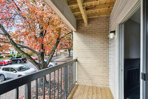 A balcony with a wooden floor and a metal railing with a view of a tree with red leaves  at Poplar Glen Apartments, Columbia, MD, 21044.