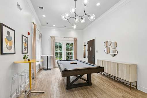 A pool table is in the middle of a room with a yellow table and a chandelier  at Poplar Glen Apartments, Columbia, MD, 21044.