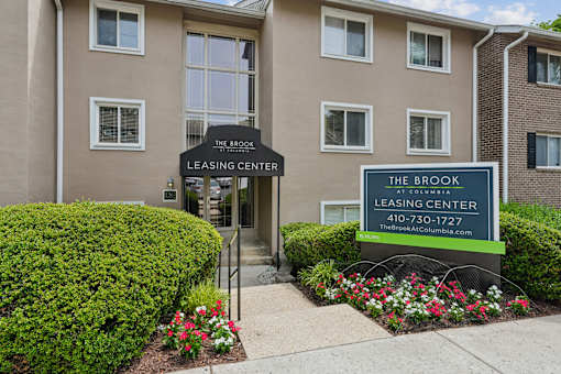 Leasing center entrance with monument sign and flowers at The Brook At Columbia Apartments, Columbia, Maryland