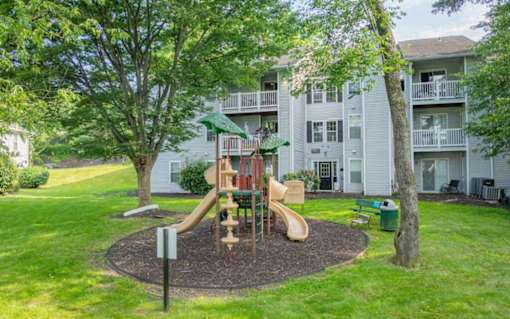 A playground with a slide and a tree in front of apartment buildings.