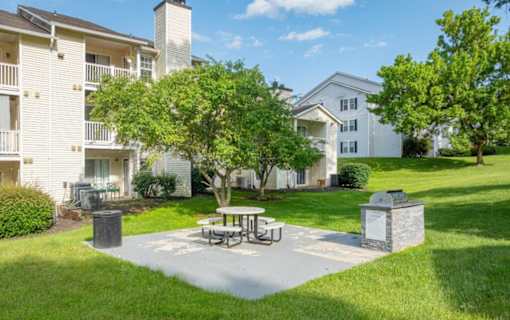 A white apartment building with a tree and picnic table in front.